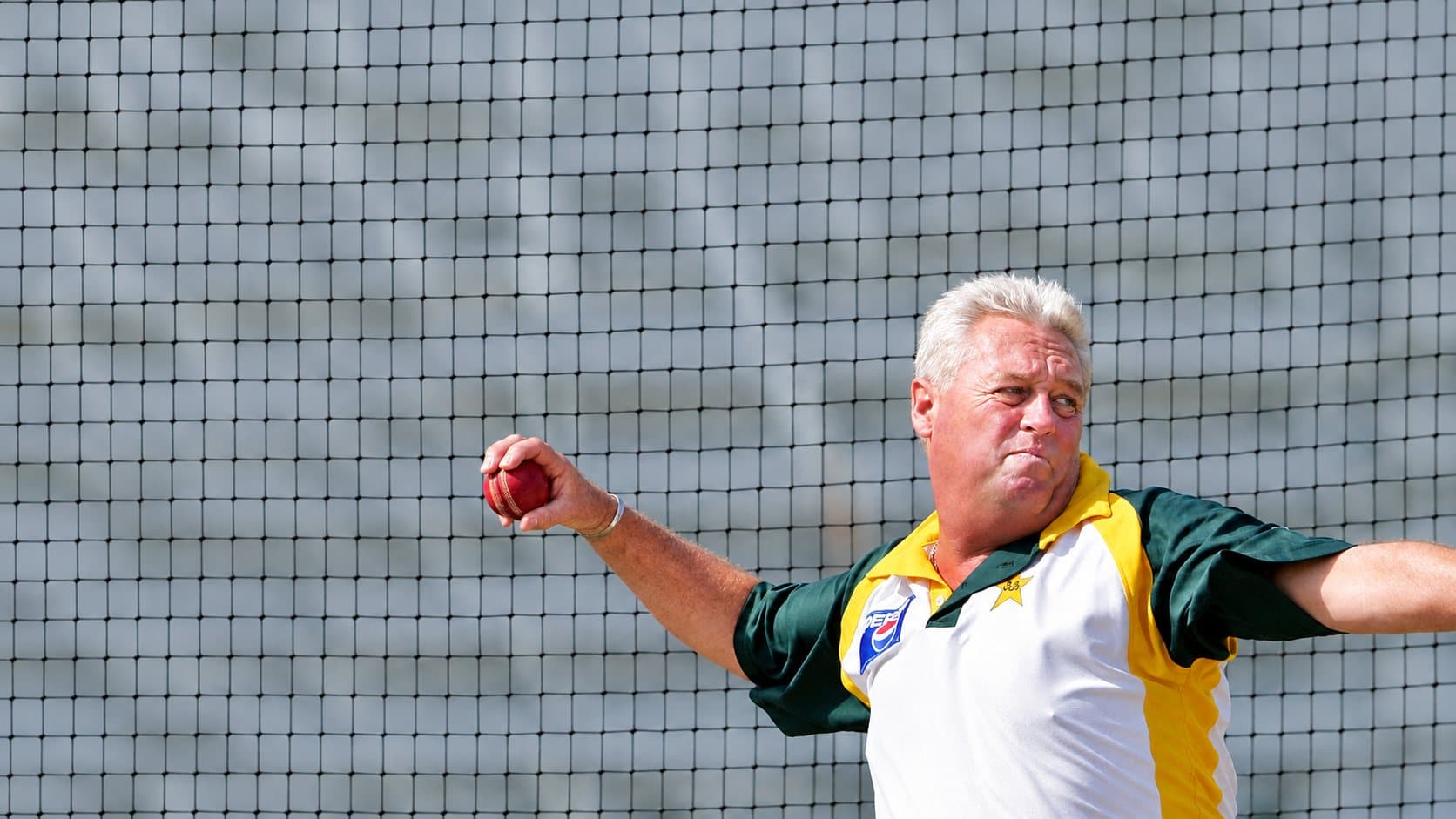 A coach bowling in the nets, mid delivery